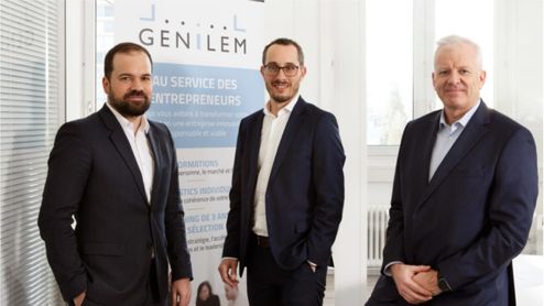 Drei Männer in Anzügen (Laurent Berney, Roland Rueff) posieren vor einem Banner von Genilem, einer Organisation im Dienste von Unternehmern, in einer hellen Geschäftsumgebung.